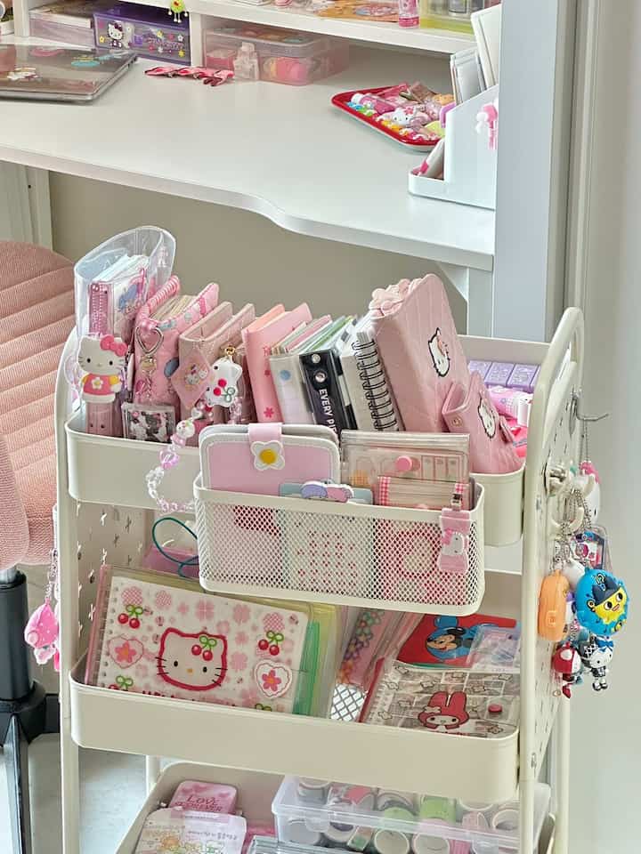 ホワイトとピンクの色調のコンパクトなホームオフィス、整理された収納トロリーとデスクが配置された居心地の良いインテリア