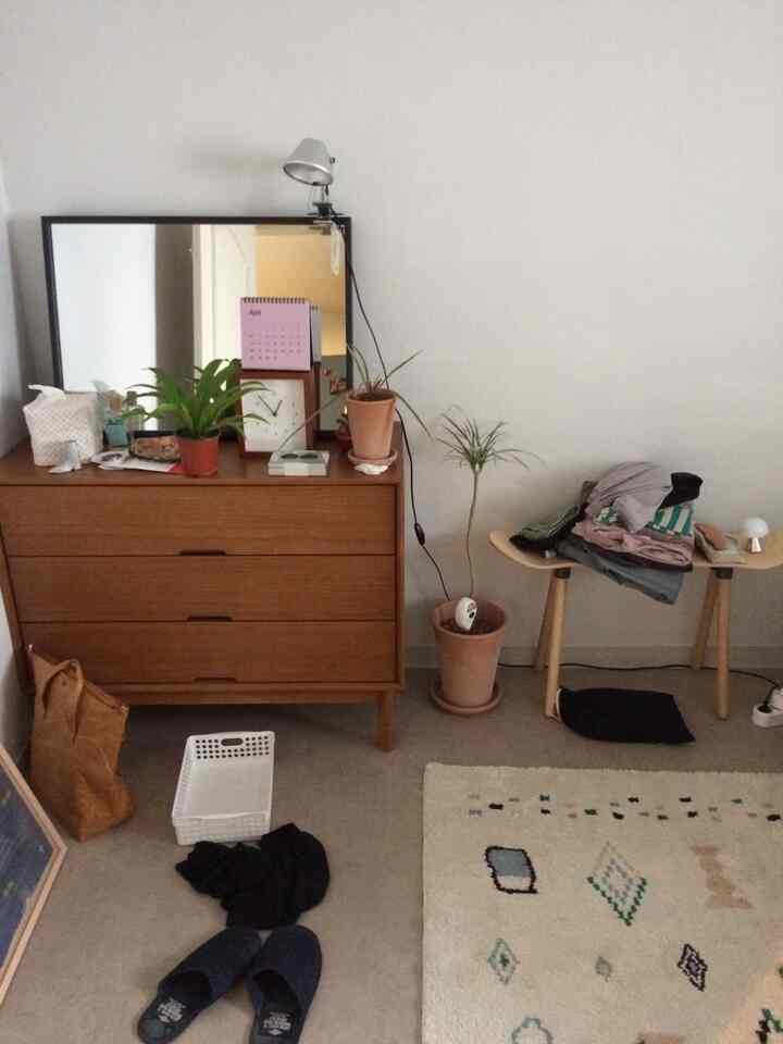 ナチュラルな色調の小さな部屋、木製のドレッサーとベンチ、植物、大きな鏡が配置されたシンプルな空間