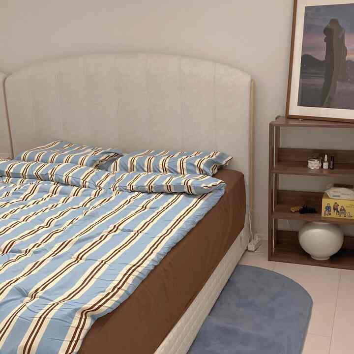 Brown and blue toned bedroom featuring striped bedding and wooden shelf, presenting a neat and natural atmosphere