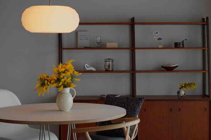 Gray-toned wall with wood-tone shelving, round dining table with yellow flowers, in a vintage style living and dining room