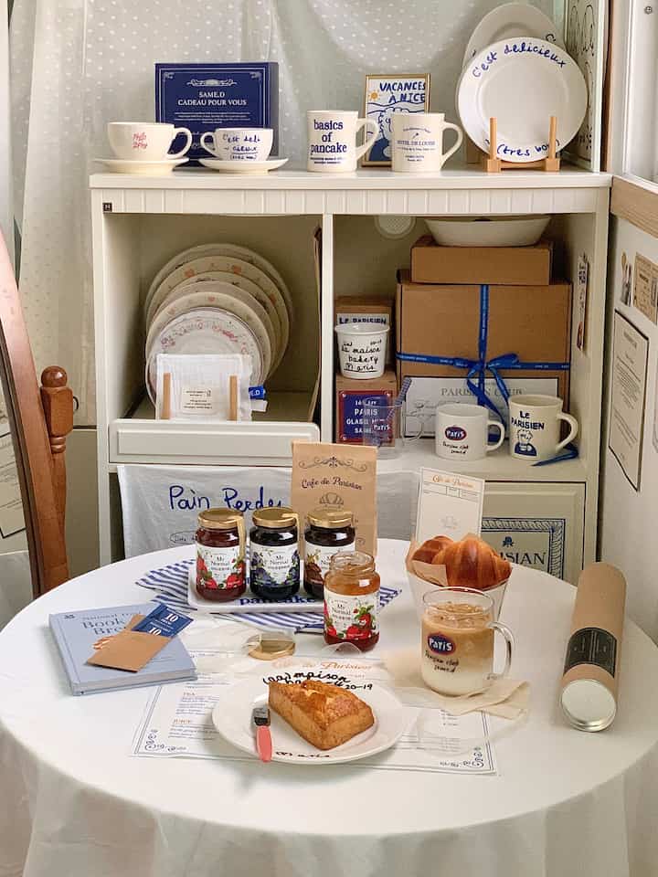 ホワイトのテーブルクロスと木製家具が配置されたベランダのおうちカフェ、皿やマグが飾られた雰囲気のあるインテリア