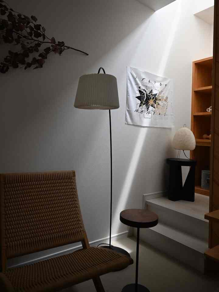 白と木目調のリビングルーム、自然素材のアームチェアとフロアランプが配置されたミニマルで落ち着いた雰囲気のインテリア