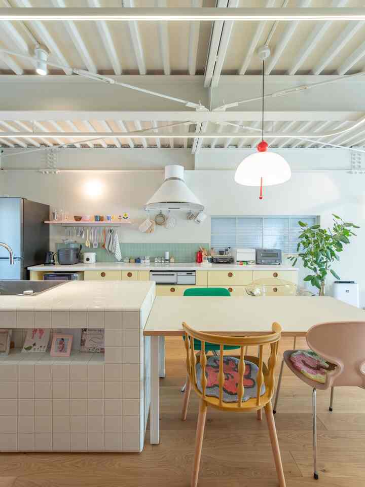 ホワイトと木目調の調和がとれたダイニングとキッチン、カラフルなチェアとペンダントライトが配置された雰囲気のある空間