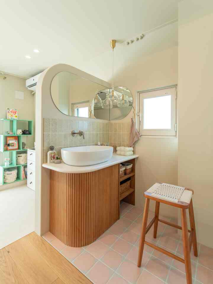 White and natural wood tone bathroom featuring a rounded mirror and wooden stool with a clean design
