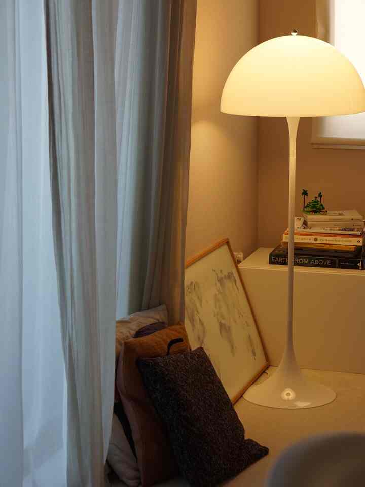 Warm beige-toned living room corner featuring floor lamp, cushions, curtains, and poster creating a cozy atmosphere