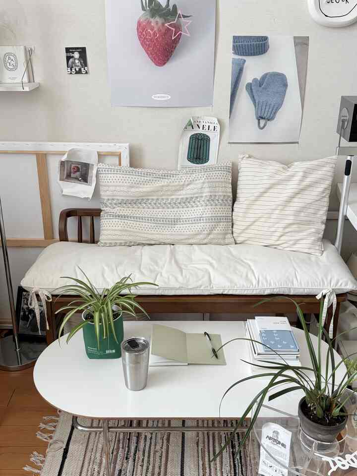 ホワイトとウッドトーンが調和したワンルームのリビング、ベンチソファとコーヒーテーブルに植物とクッションが配置されたシンプルで自然な雰囲気のある空間