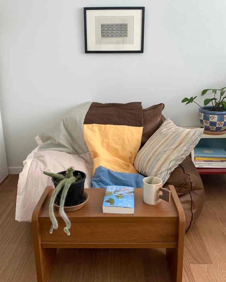 ナチュラルトーンの小さな部屋にブラウンレザーのビーズソファ、木目調のサイドテーブル、パッチワークのブランケットが配置されたインテリア