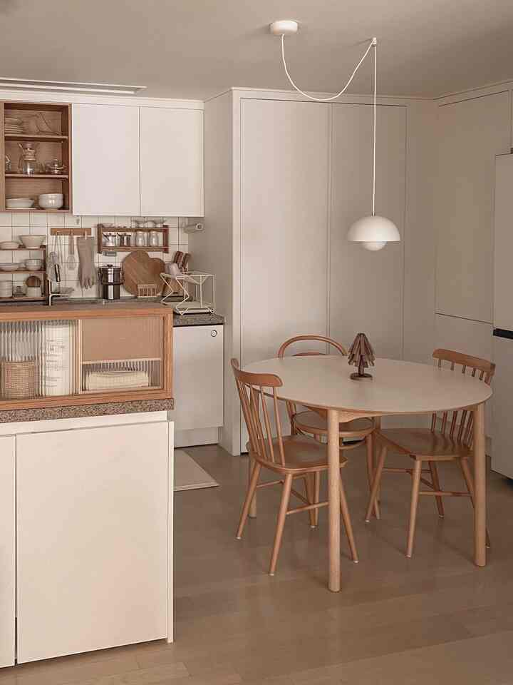 ナチュラルな木目調と白のキッチン、丸いダイニングテーブルと木製の椅子が配置された雰囲気のある空間