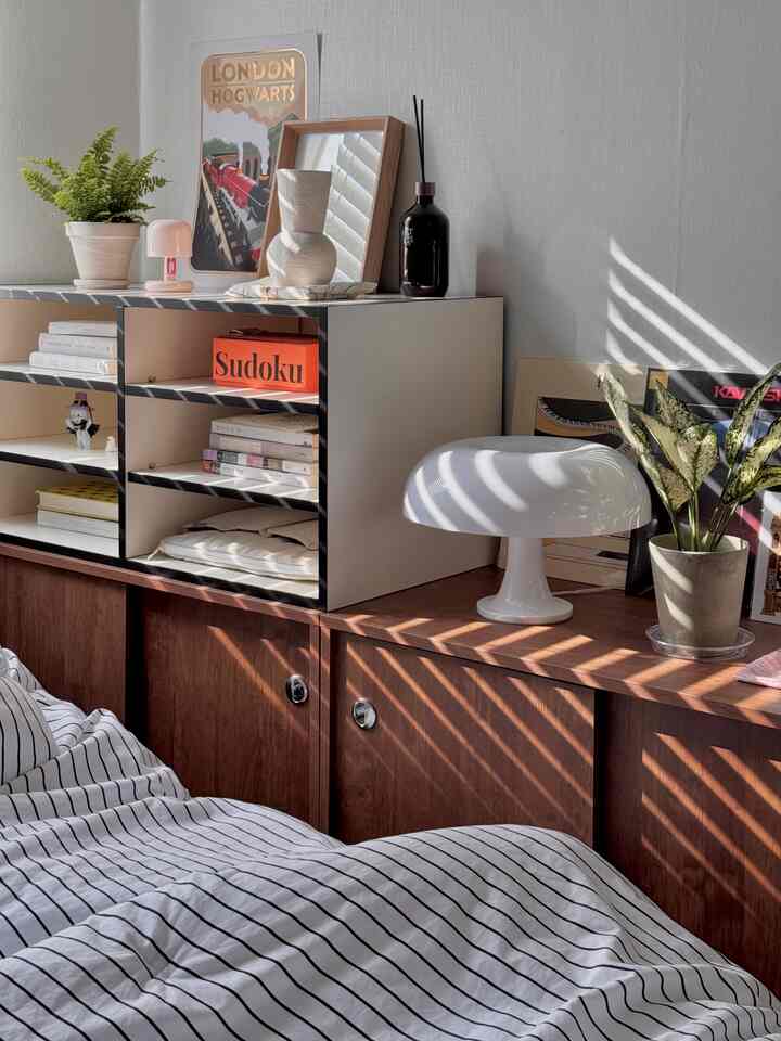 白と茶色のトーンの寝室、ブラインド越しに朝日が差し込み、ベッドカバーとチェストに温かみのある雰囲気を作るインテリア