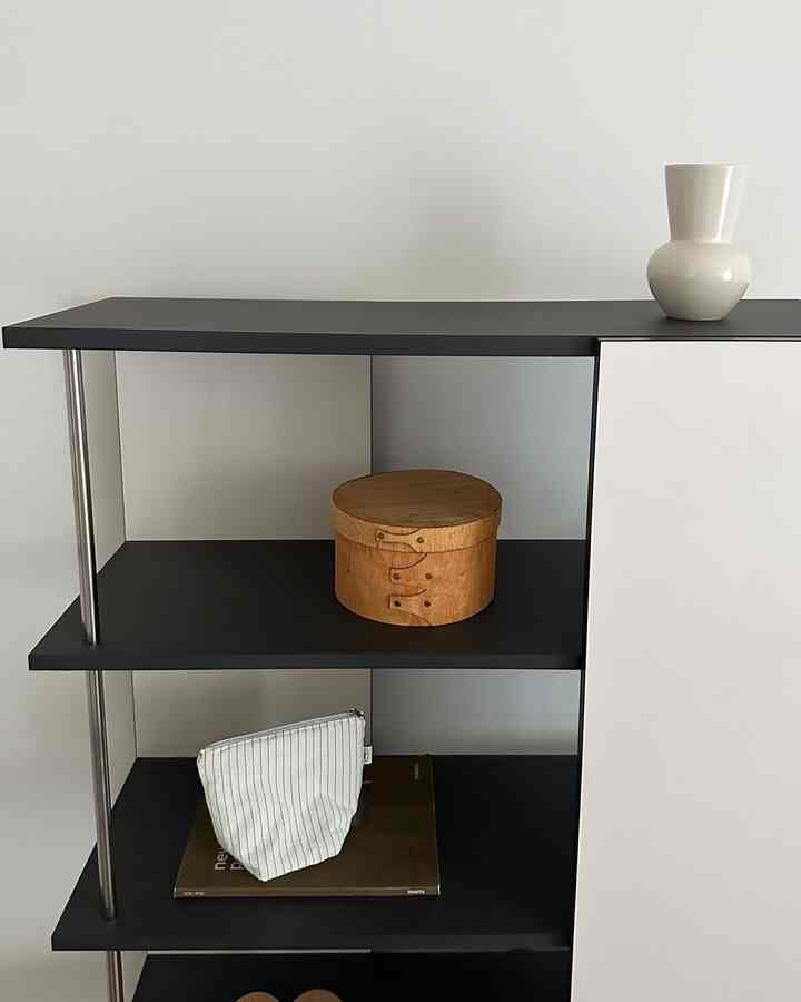 白い壁とナチュラルな木製オブジェが置かれたシンプルな黒い棚のインテリア