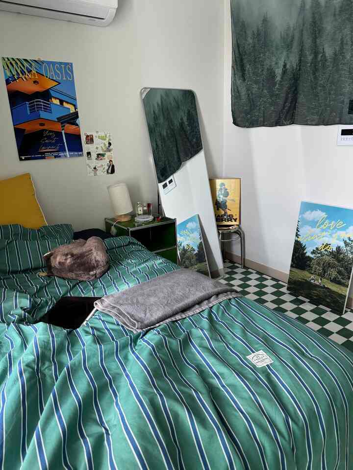 緑とネイビーのトーンでまとめた5坪のワンルーム寝室、ストライプの寝具とナイトテーブル、大きな立てかけ鏡が配された落ち着いた空間