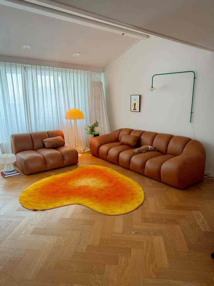 ナチュラルな木目調の床に温かみのあるブラウンのソファ、鮮やかな黄のラグと調和のとれた照明が配置されたリビングルーム