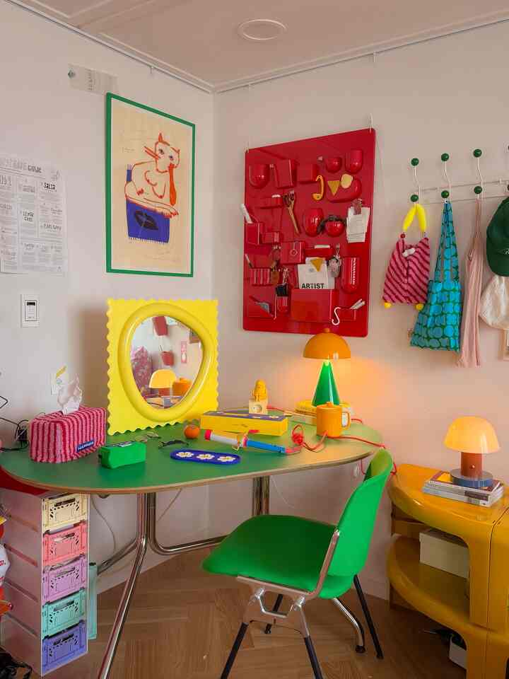 カラフルな色調のワンルームホームオフィス、緑のデスクと椅子、黄色の鏡と装飾が配置された雰囲気のある作業空間