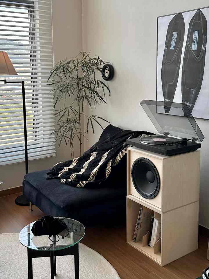 白い壁と大きな白いウッドブラインドのあるスタジオアパート、黒の一人用ソファとターンテーブルが配置されたミッドセンチュリーモダンなインテリア