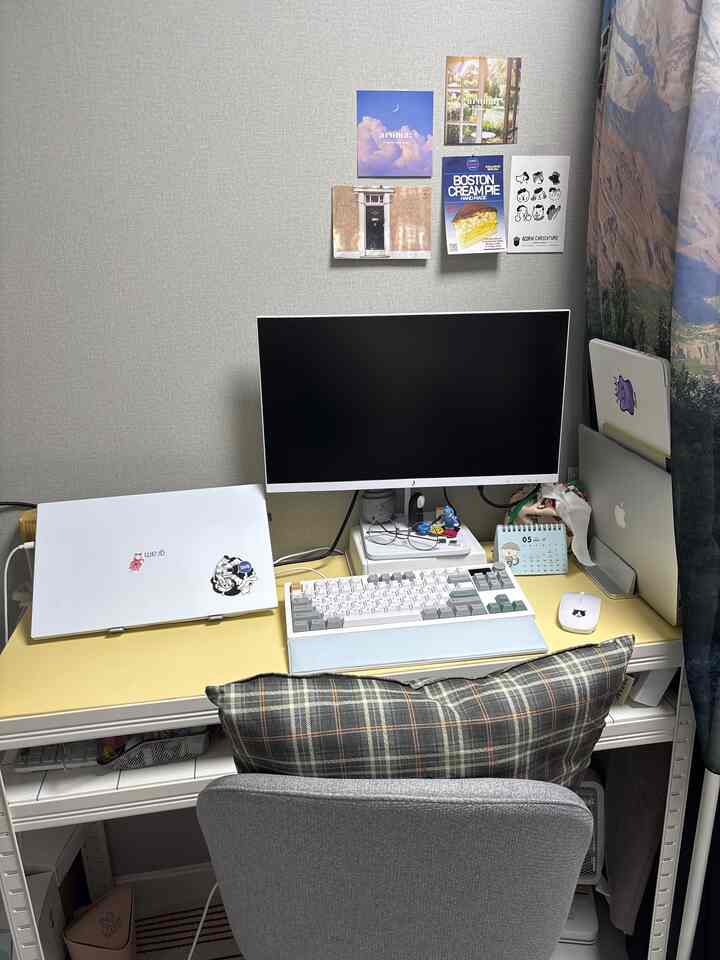 黄色のデスクとグレーの椅子が配置されたコンパクトなホームオフィス、壁に多彩な絵が飾られた雰囲気のあるインテリア
