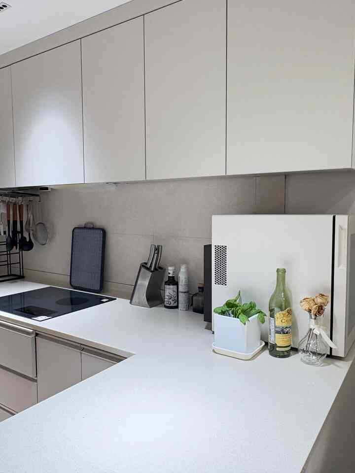 ベージュとグレーのトーンのモダンなキッチン、すっきりとしたカウンターにバジルの鉢とドライフラワーが配置された雰囲気のあるインテリア