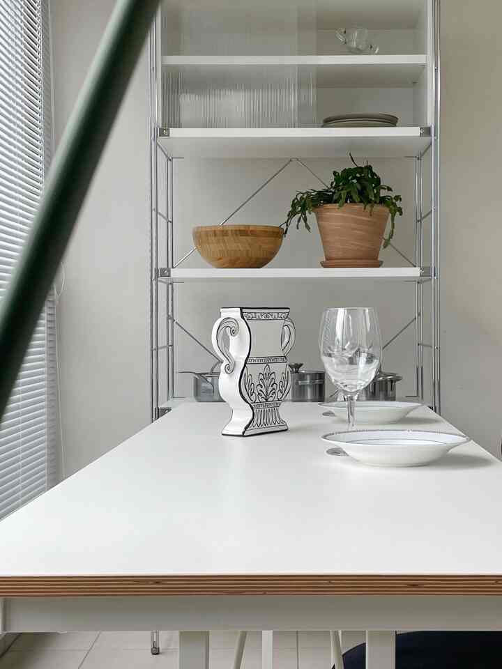 白とナチュラルカラーが調和するダイニングルーム、シンプルな棚とテーブルの食器が配置された雰囲気のある空間