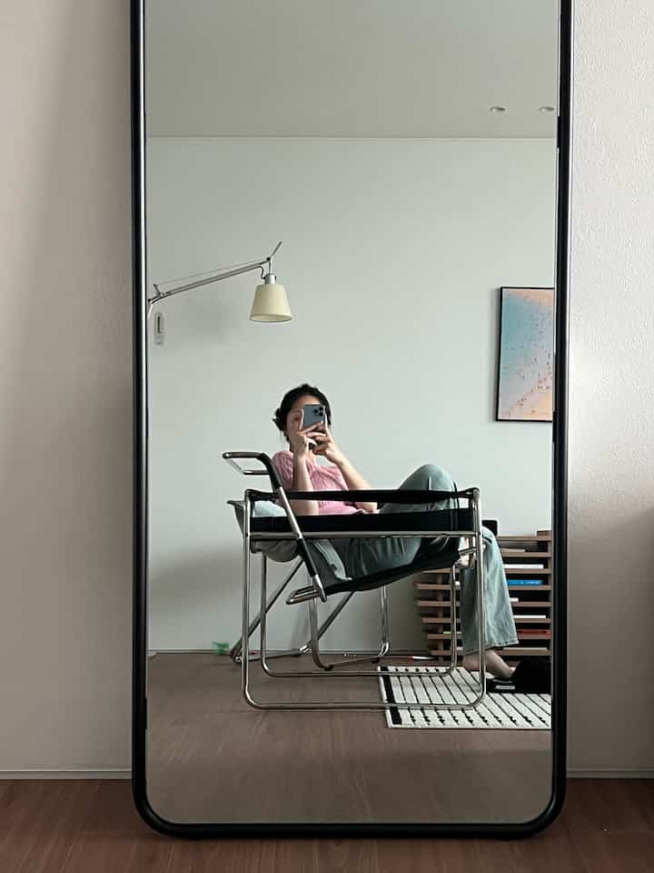 ナチュラルモダンなリビング、印象的な大きな全身鏡とキャットトイ、フロアランプ、本棚が配置されたシンプルな空間