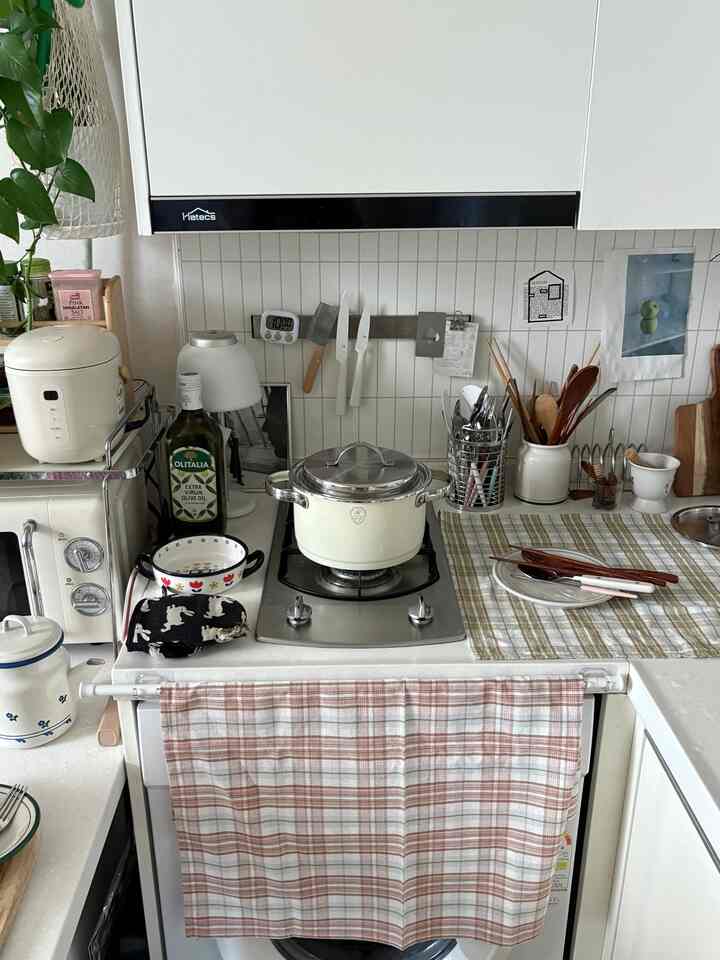 白を基調としたブラウンのキッチン、チェック柄のキッチンタオルと多様な調理器具が配置された雰囲気のあるヴィンテージスタイルの空間