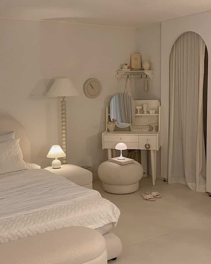 アイボリーとベージュの色調の寝室、化粧台とスツール、柔らかな照明が配置された雰囲気のあるインテリア