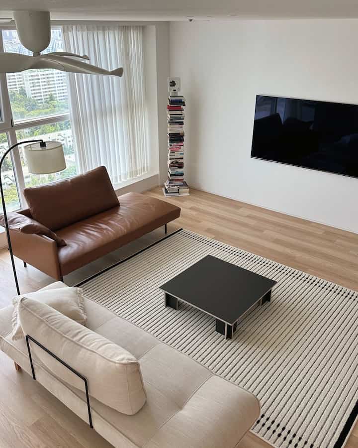 Living room with white walls and wood-tone flooring, featuring modern leather and fabric sofas with a coffee table in a neat arrangement
