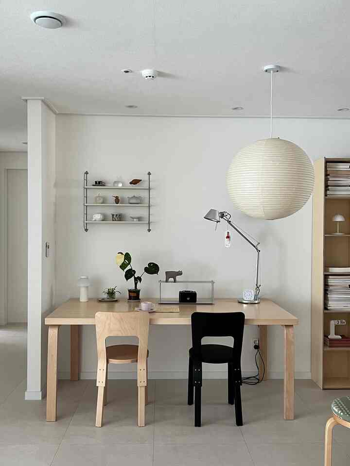 ナチュラルカラーのダイニングルーム、明るい木製テーブルと黒い椅子、ペンダントライトとテーブルランプが配置されたモダンな雰囲気のインテリア