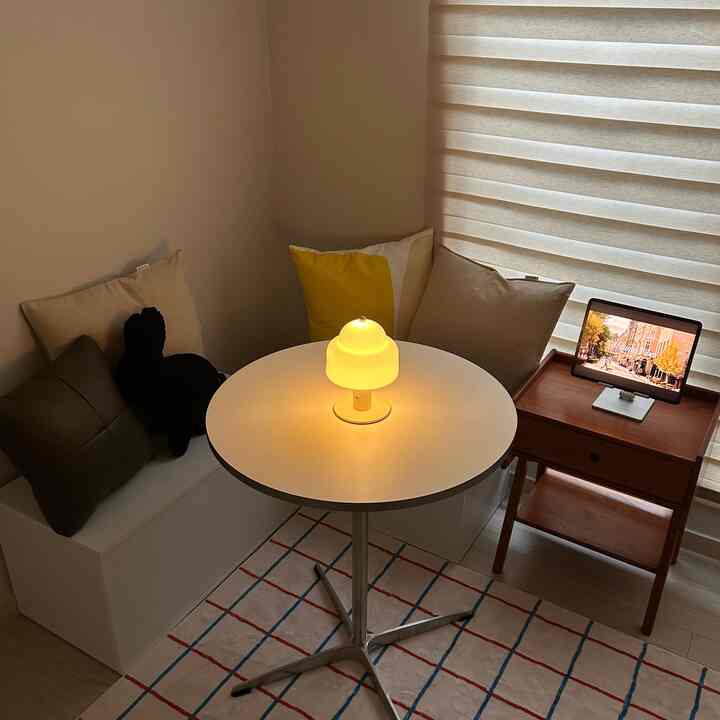 白と木目調が調和する小さな書斎、丸テーブルのランプが温かみのある雰囲気を醸し出すインテリア