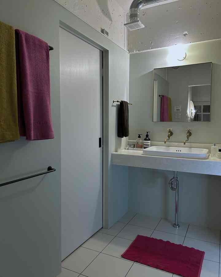 白と淡いミント色の壁のバスルーム。ピンクのタオルとバスマットがアクセントのホテルライクな空間