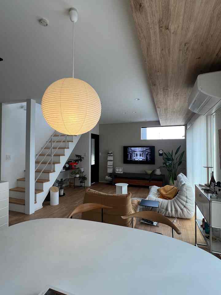 ナチュラルな色調のリビング、ホワイトソファと丸いペンダントライトが配置されたミニマルな印象的な空間