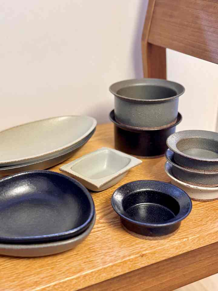 Natural wood-tone chair displaying assorted ceramic pottery plates and bowls, creating a simple dining room vibe