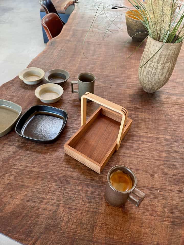Natural wood tone long table featuring pottery plates, cups, and a wooden tray creating a cozy home cafe setting