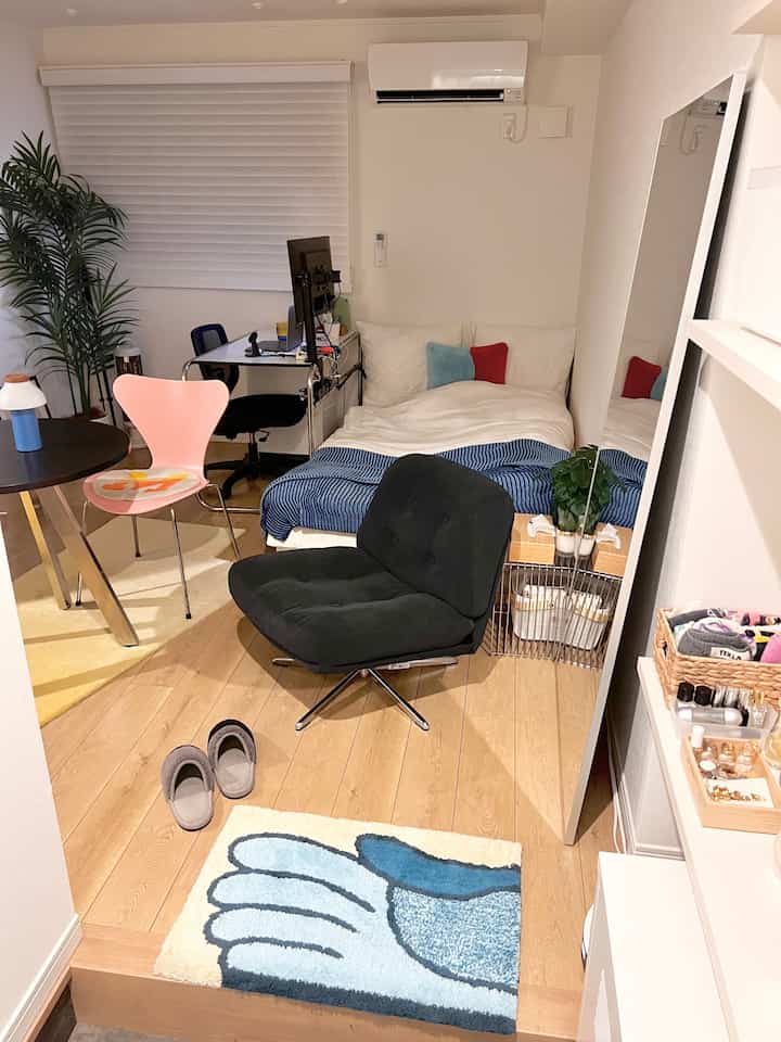 White and wood tone studio apartment bedroom featuring a compact layout with desk, armchair, and bed in mid-century modern style interior