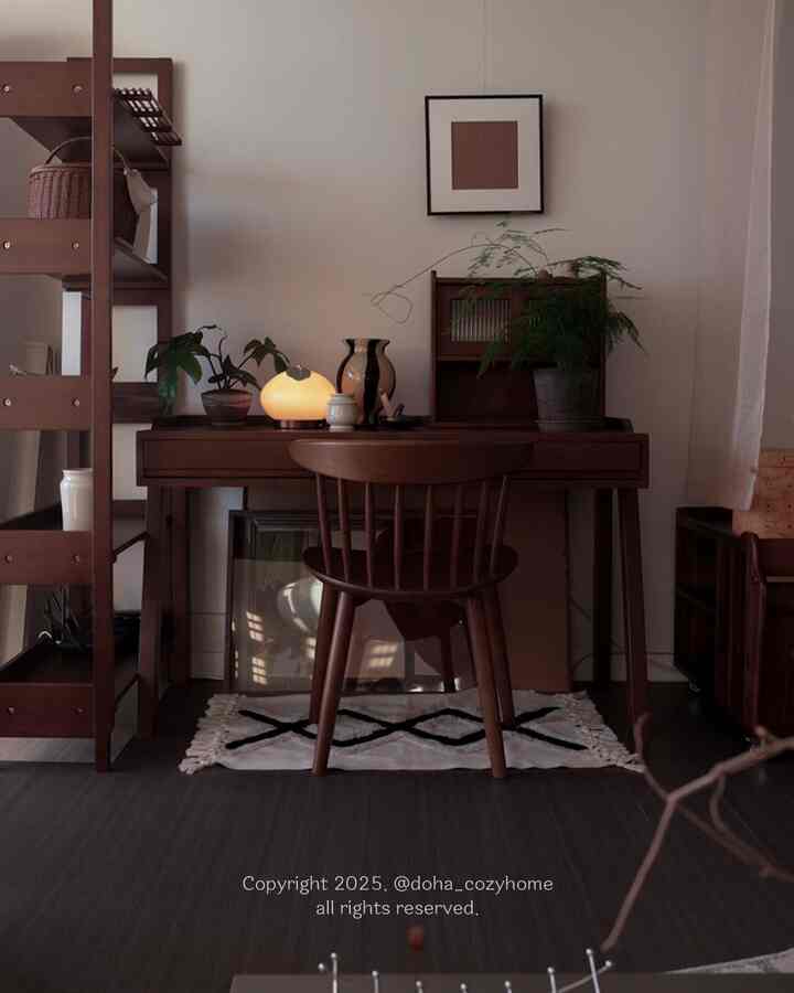 A warm natural tone home office space featuring a wooden desk and chair with lighting, plants, and Art Deco wall art