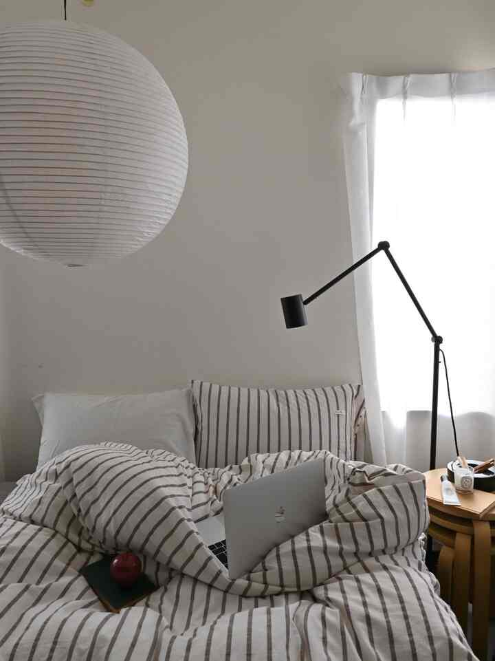 白と茶色のトーンの寝室、ストライプの掛け布団カバーとフロアランプが配置された自然な雰囲気のインテリア