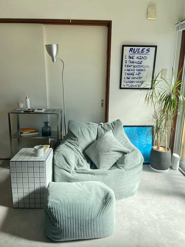 Soft mint green bean bag sofa with ottoman, metal shelf, plant, and floor lamp in a cozy mid-century modern living room space