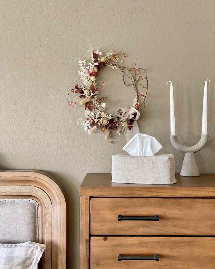 Beige-toned wall decorated with a round wreath in a natural style bedroom, featuring wooden dresser and candle holder for a cozy atmosphere
