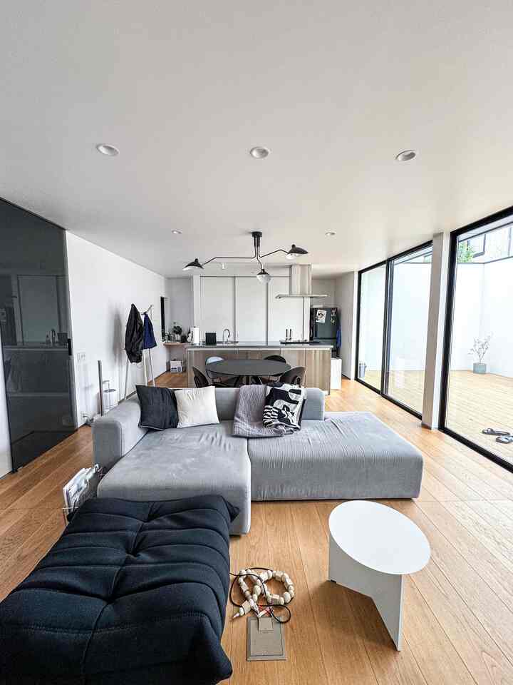 白と木目調のモダンなリビング、大きな窓とグレーのソファが配置された雰囲気のある空間