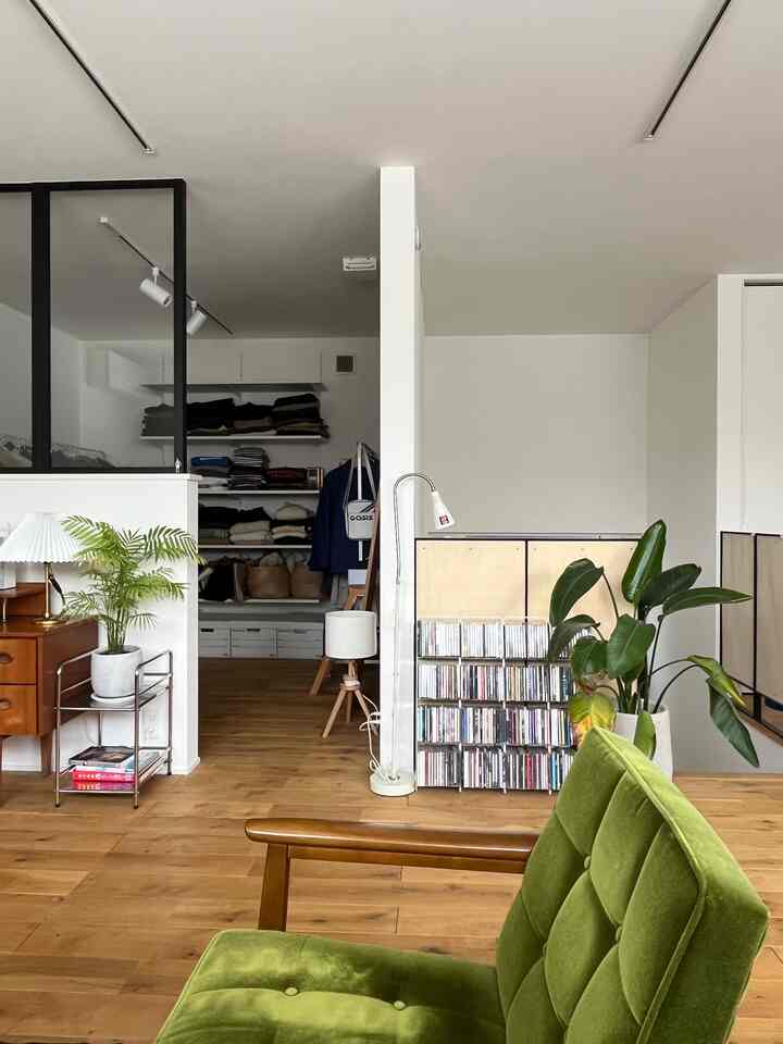 白い壁と木目調の床のリビング、ヴィンテージとミッドセンチュリースタイルの家具、緑のアームチェアとフロアランプが配置された雰囲気のあるインテリア