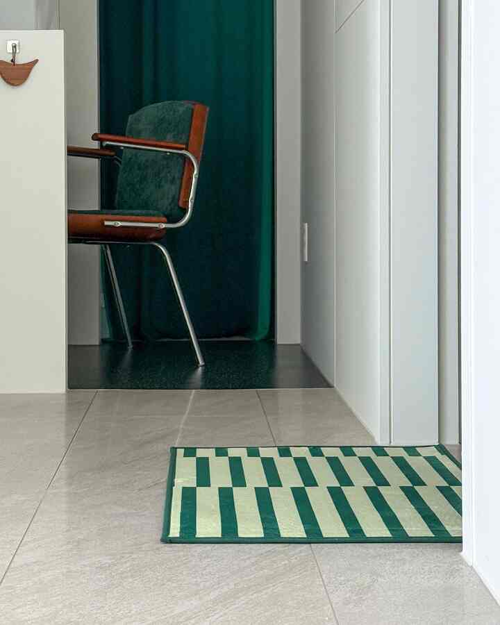 緑と白のトーンの玄関、モダンなアームチェアとパターンドドアマットが配置された洗練されたインテリア