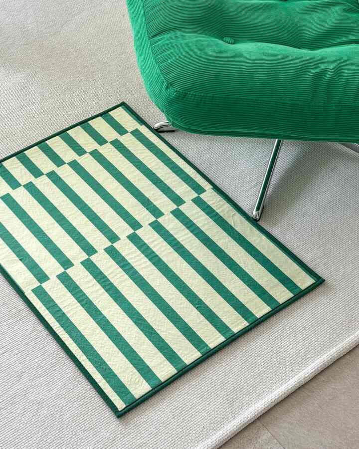 Modern entrance area featuring a green fabric armchair and a door mat with vivid yellow-green stripes creating a fresh spring atmosphere