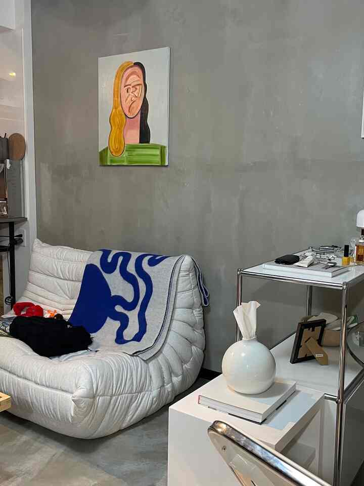 グレーのコンクリート壁と白いソファが配置されたミニマルでアート感のある一人暮らしのリビング