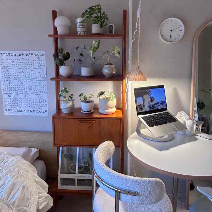 白い壁と茶色の木製収納があるナチュラルなホームオフィス空間、白い丸テーブルにノートパソコンとクッションチェアが配置されている
