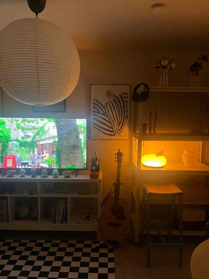 暖かいオレンジ色の照明と白い壁のモダンなリビング、ギターとチェッカーボードラグが配置された落ち着いた空間