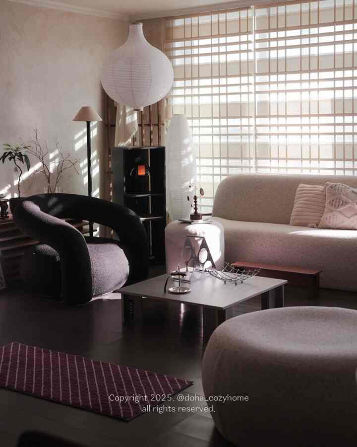 A modern living room in soft white, black, and wood tones, featuring low-profile furniture and cushions creating a cozy atmosphere