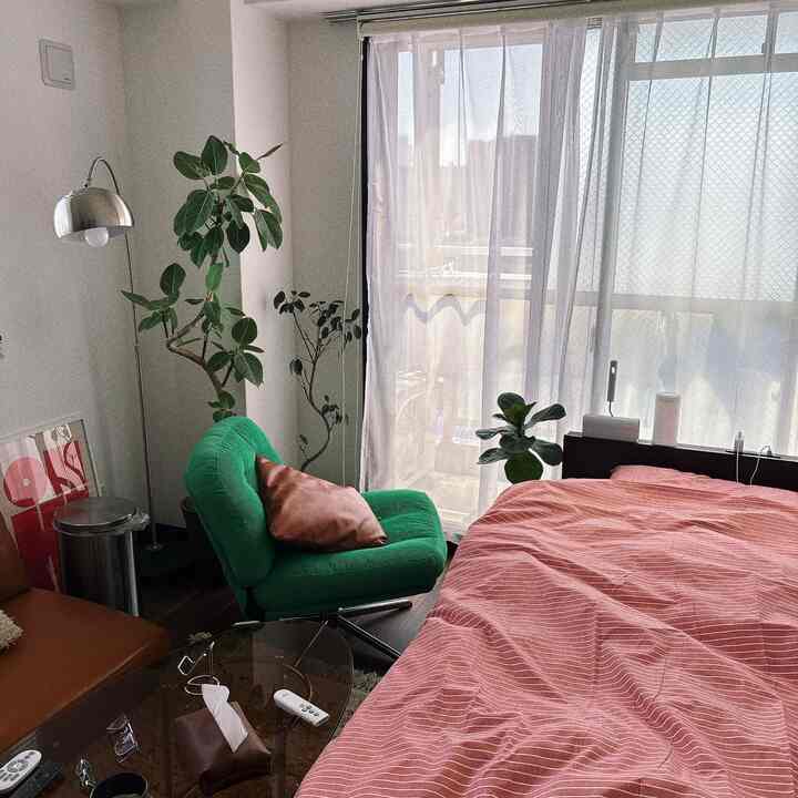 ナチュラルな雰囲気の8畳ワンルーム寝室、緑のアームチェアと赤い掛け布団カバー、植物が配置された落ち着いたインテリア