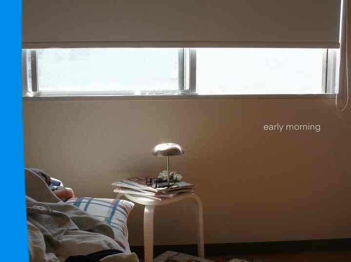 A narrow single-occupant bedroom with calm beige walls and a white table lamp on a side table