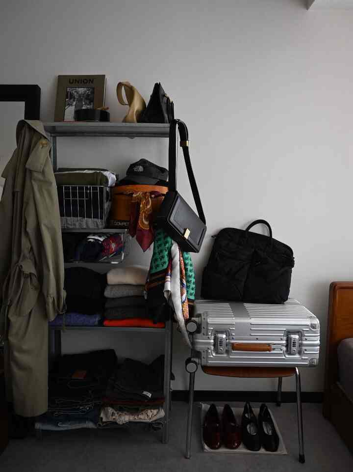 Gray-toned metal shelving with neatly folded clothes, bags, and a suitcase in a simple storage space