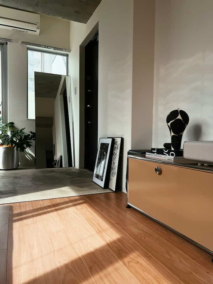 Modern entrance space with white walls, wood-tone floor, large floor mirror, and sunlight by the doorway