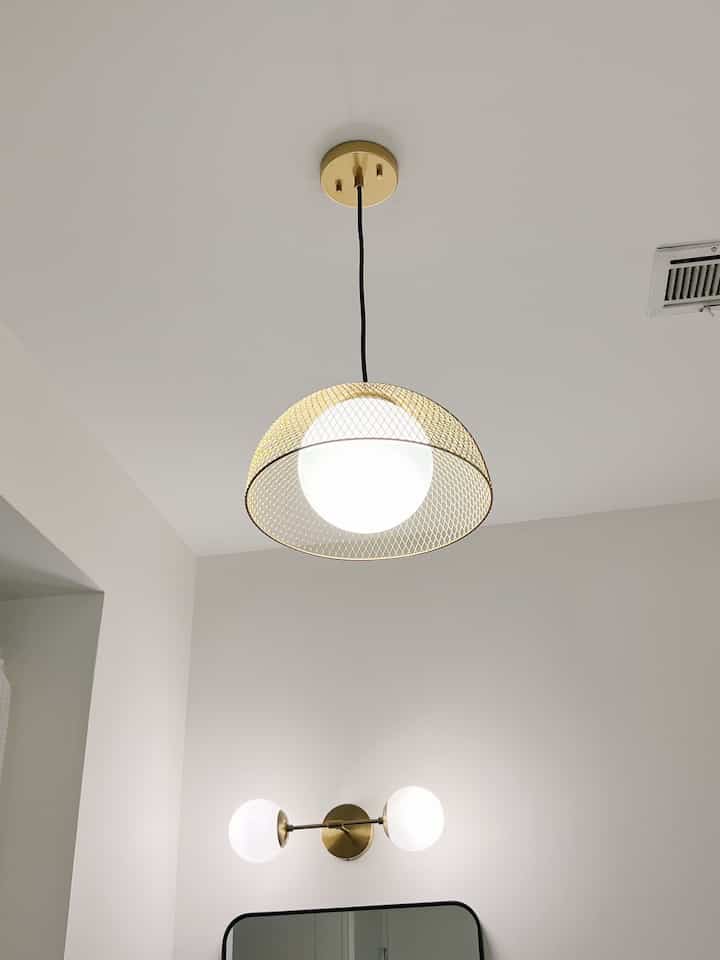 White and gold toned bathroom featuring mid-century modern pendant light and wall sconces with clean minimal design