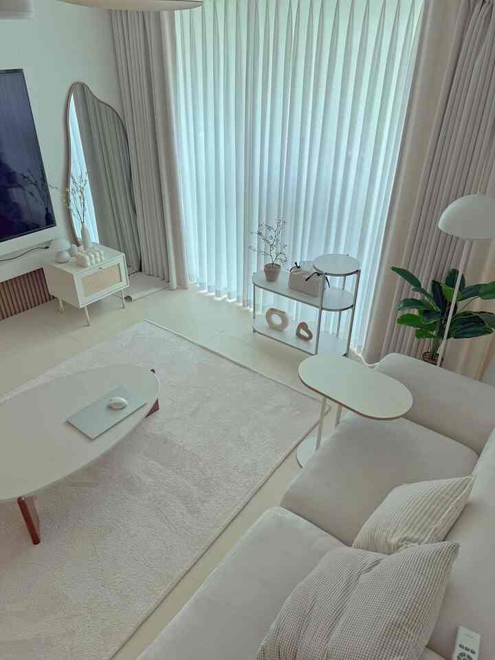 明るいホワイトトーンのリビング、ソファとコーヒーテーブル、カーテンと植物が配置されたナチュラルモダンなインテリア